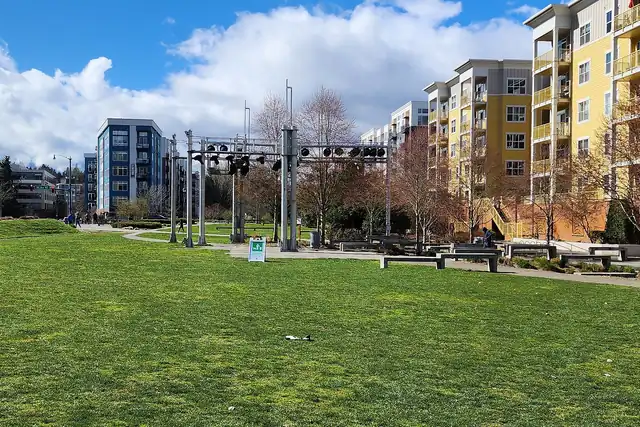 A wide green lawn under a blue sky with white clouds, with a row of tall steel frames across the middle.