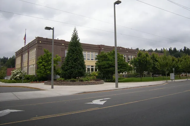 A long two-storey brick school building with rows of tall windows and a flagpole in front.
